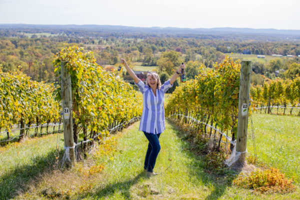 Virginia Wine Club owner Loree Rupy in the vineyard holding wine bottles